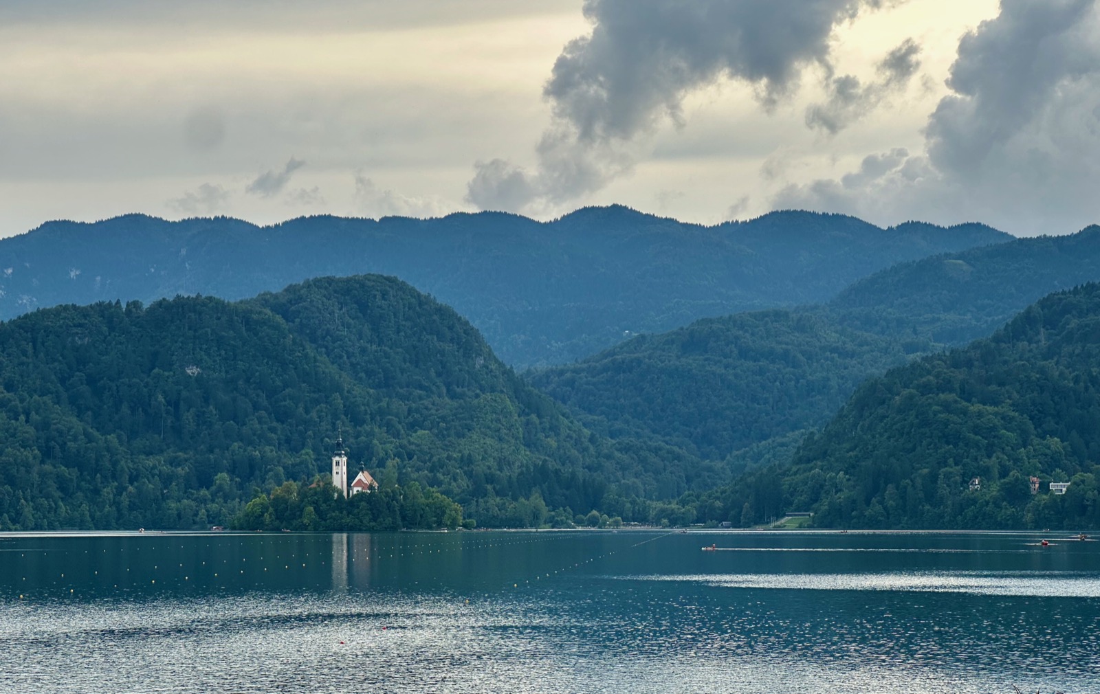 Bled's iconic church perched on a lake island captivates amidst lush, mountainous Slovenian scenery.