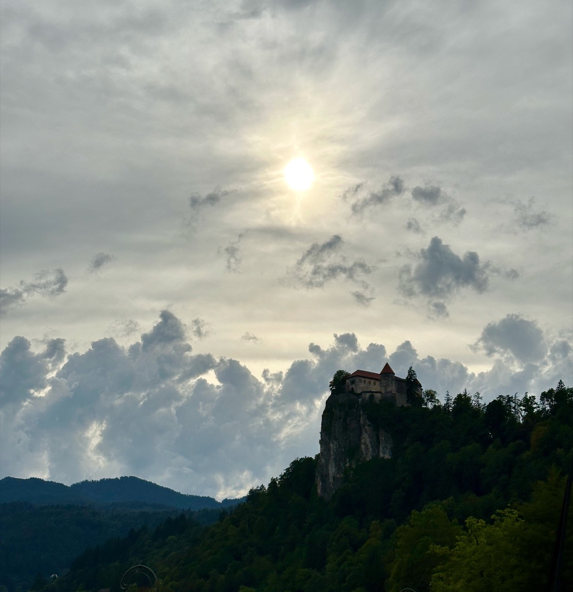 Castle on rocky cliff under cloudy sky.