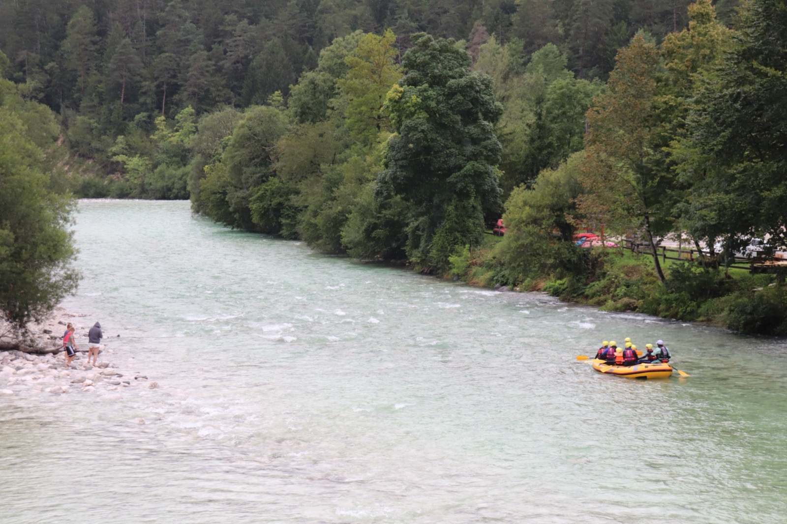 Yellow raft with four people wearing helmets and life jackets on a river with trees and rocks.