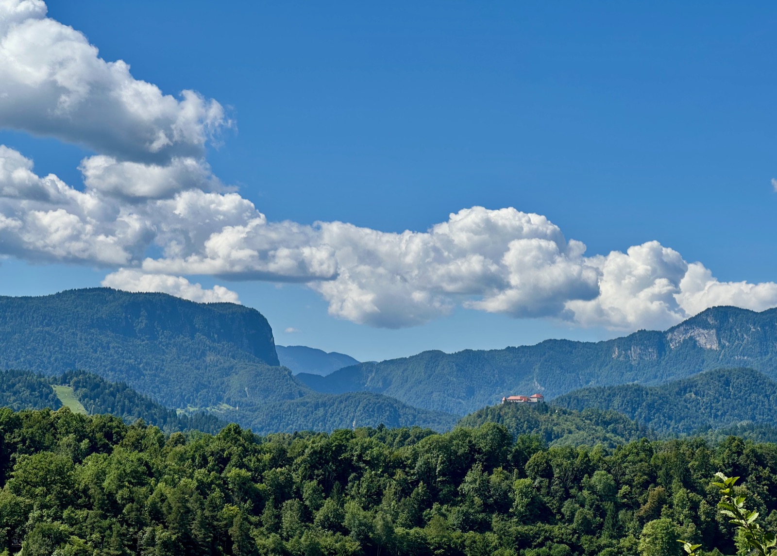 Clouds over forested mountains and a red building.