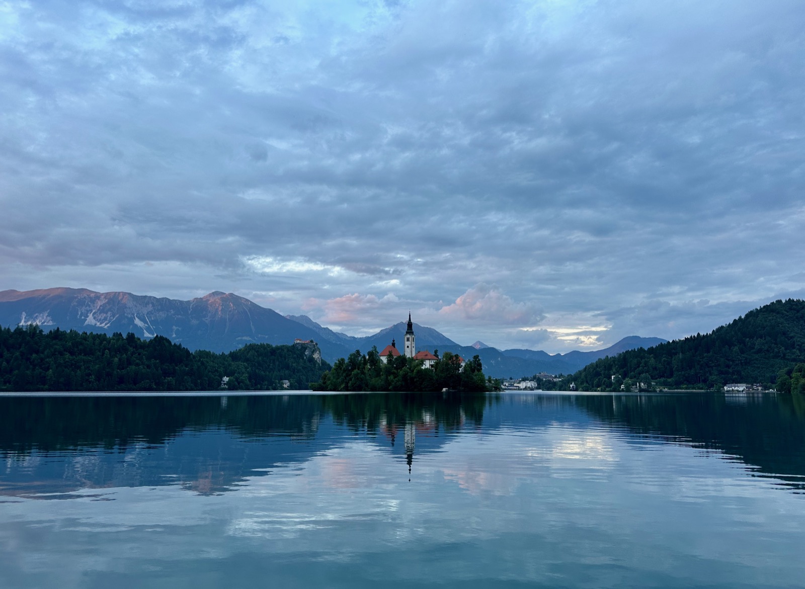 Bled, Slovenia's iconic church island glistens under a dramatic, cloud-streaked sky at dusk.