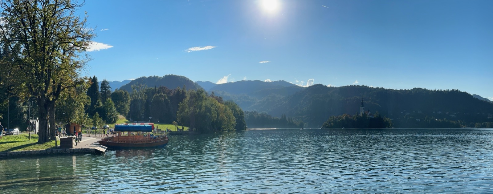 Wooden boat docked at grassy shore with trees and mountains in background.