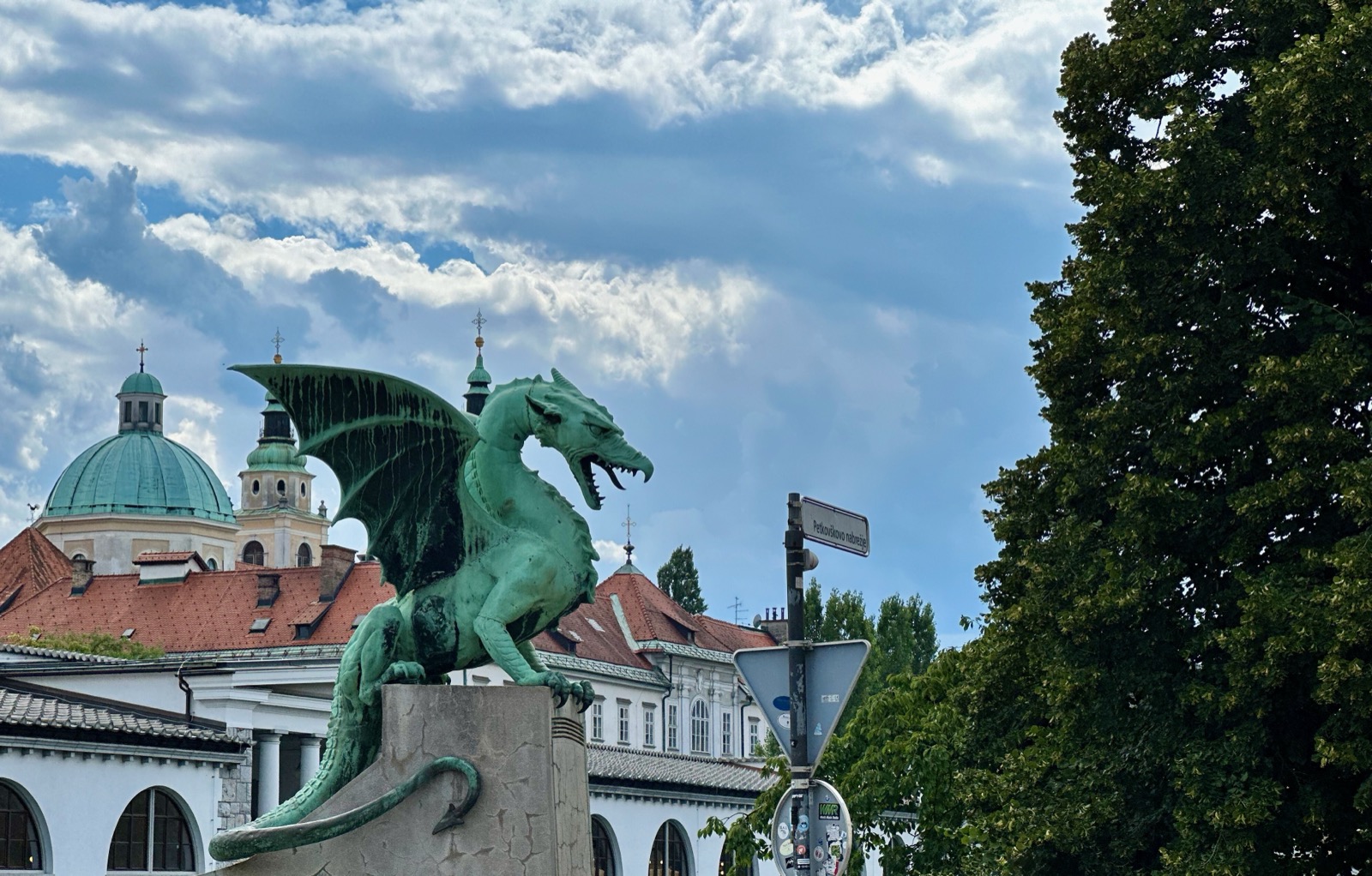 Green dragon statue on stone pedestal near buildings under cloudy sky.