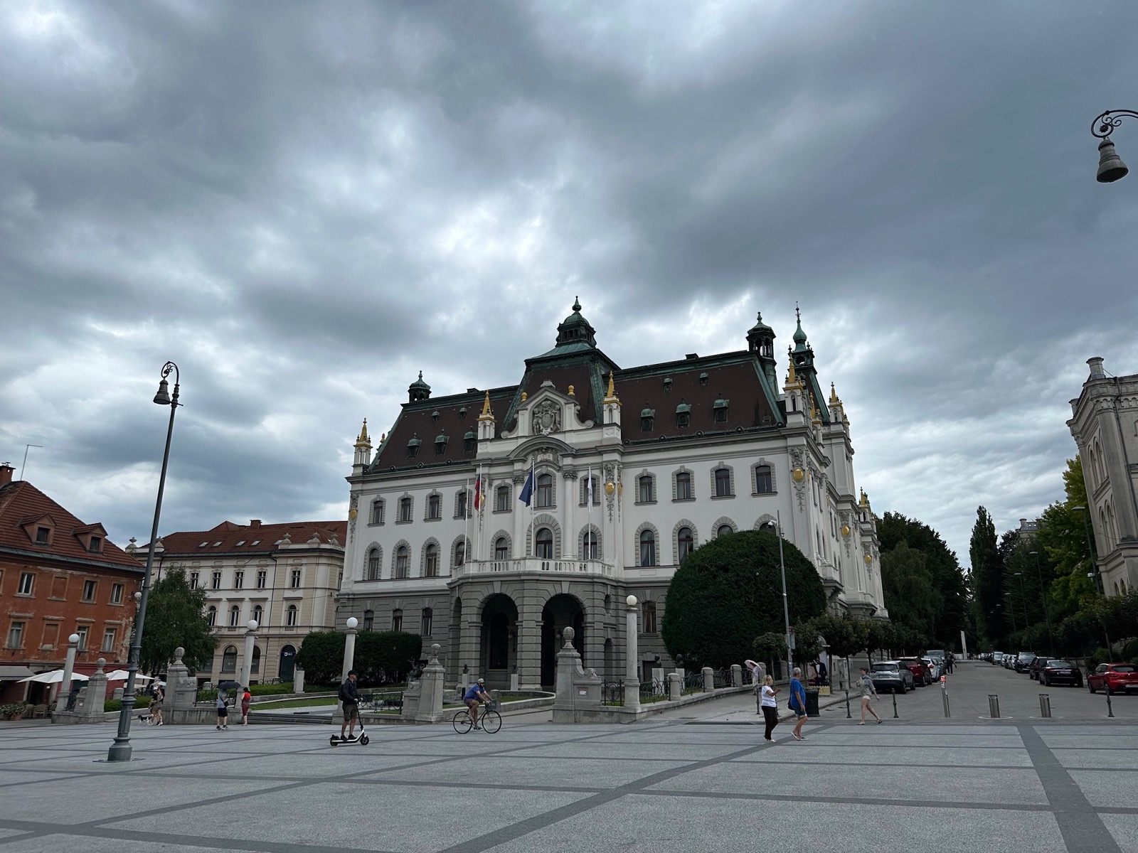 White building with flags, statues, and people in front of gray sky.
