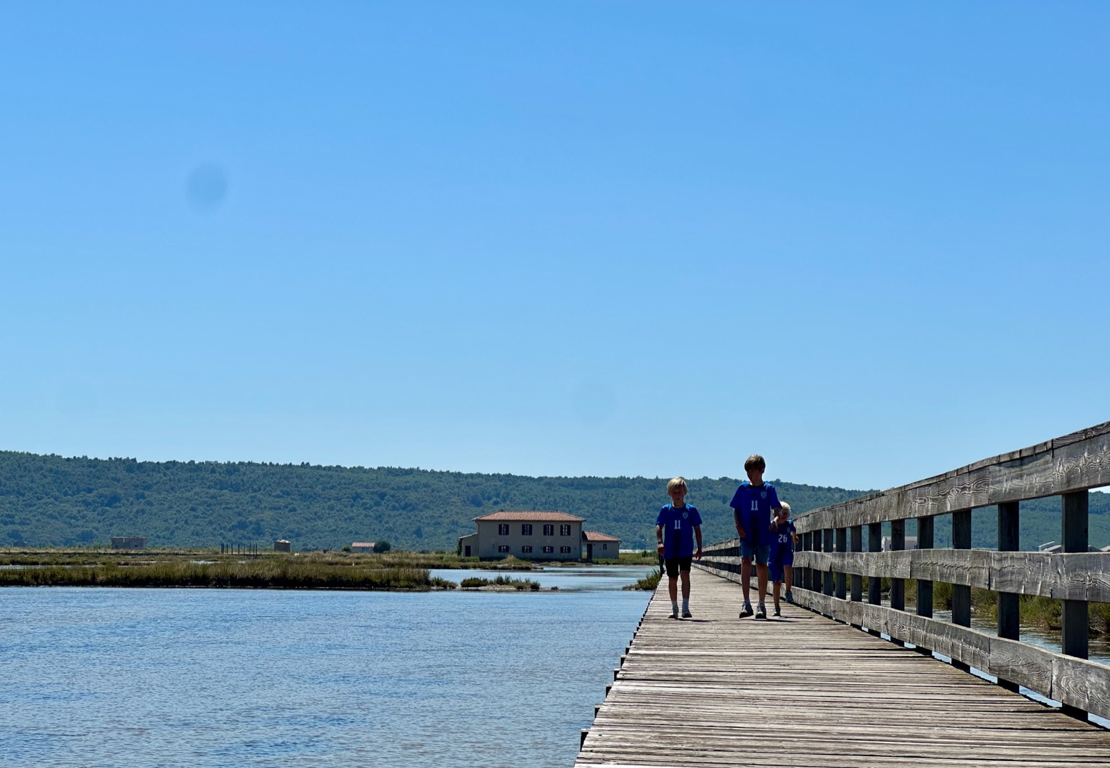 Two children in blue jerseys walking on a wooden pier.