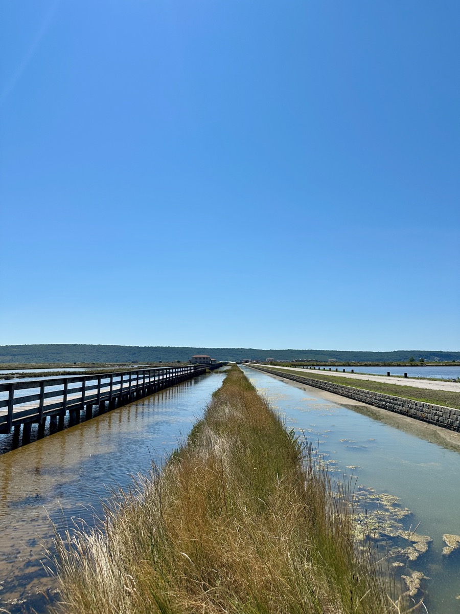 Wooden pier beside water canal with grass and hills in background.