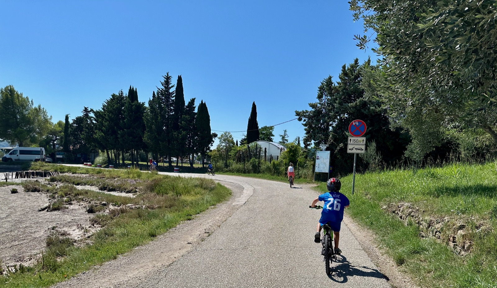 Child in blue jersey riding bicycle on rural road with sign and trees.
