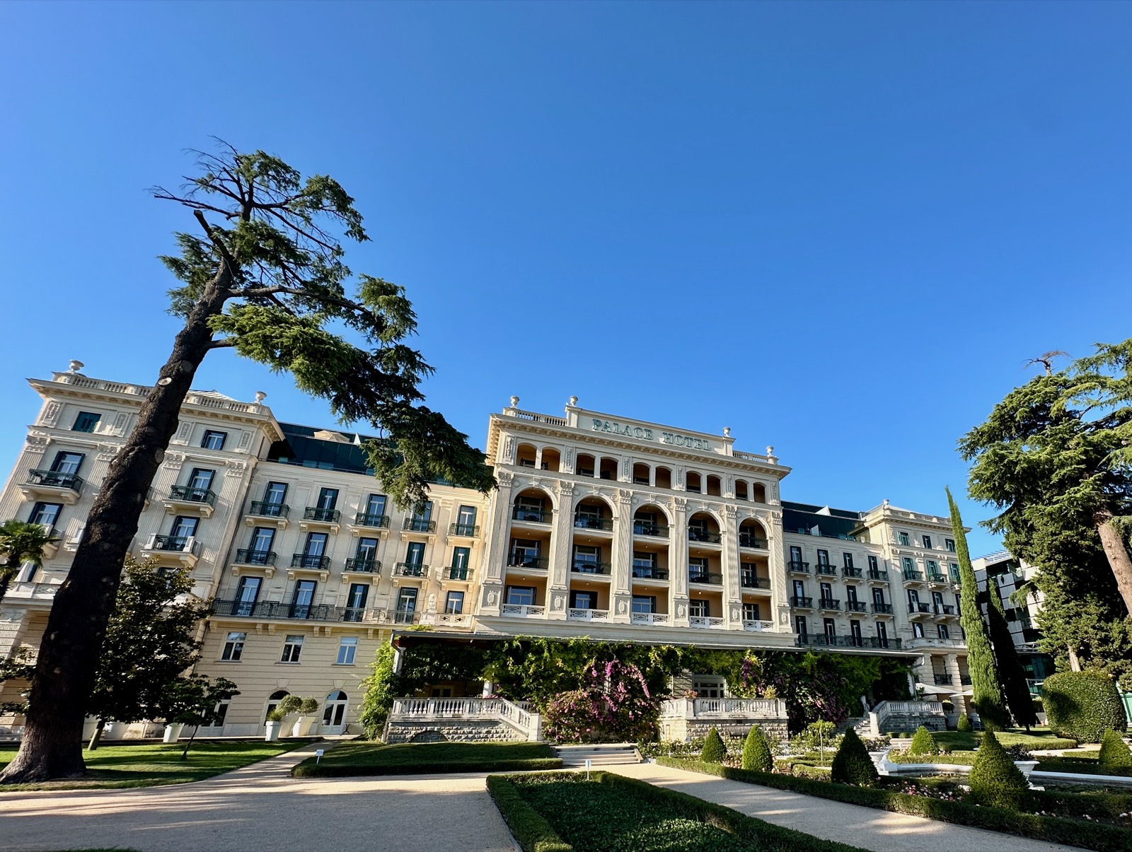 White building with balconies, arches, and trees under blue sky.