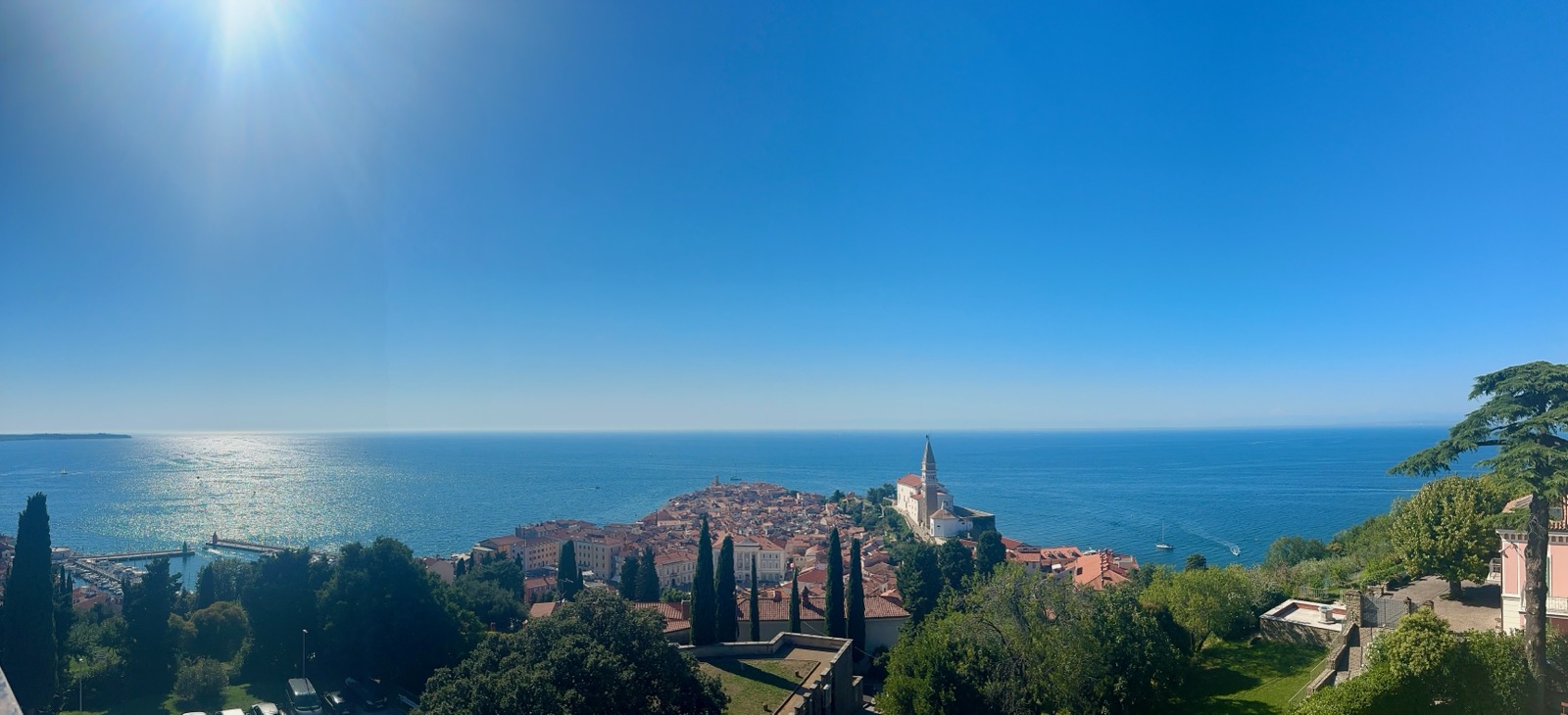 A coastal town with red-roofed buildings, a church, and trees overlooking the sea.