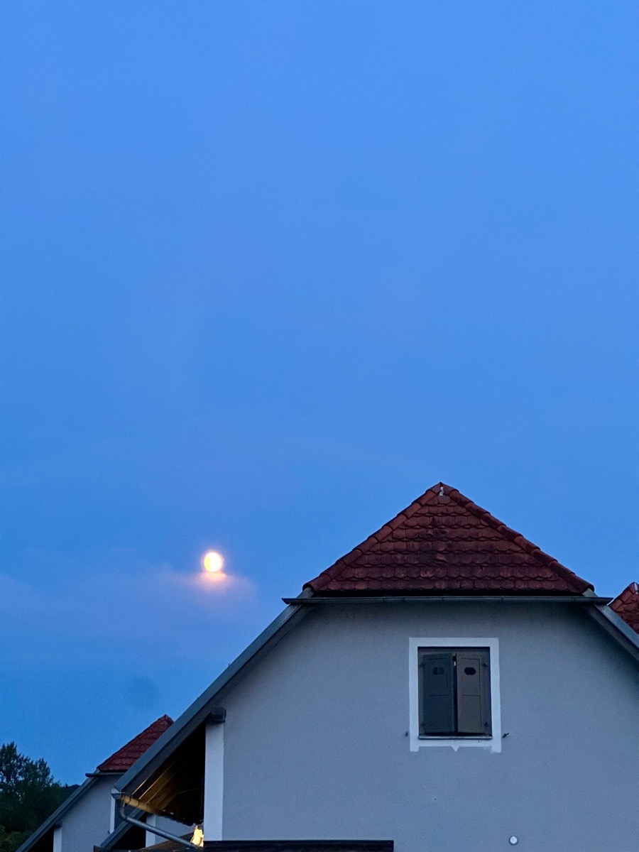 A house with a red roof under a blue sky with a moon.